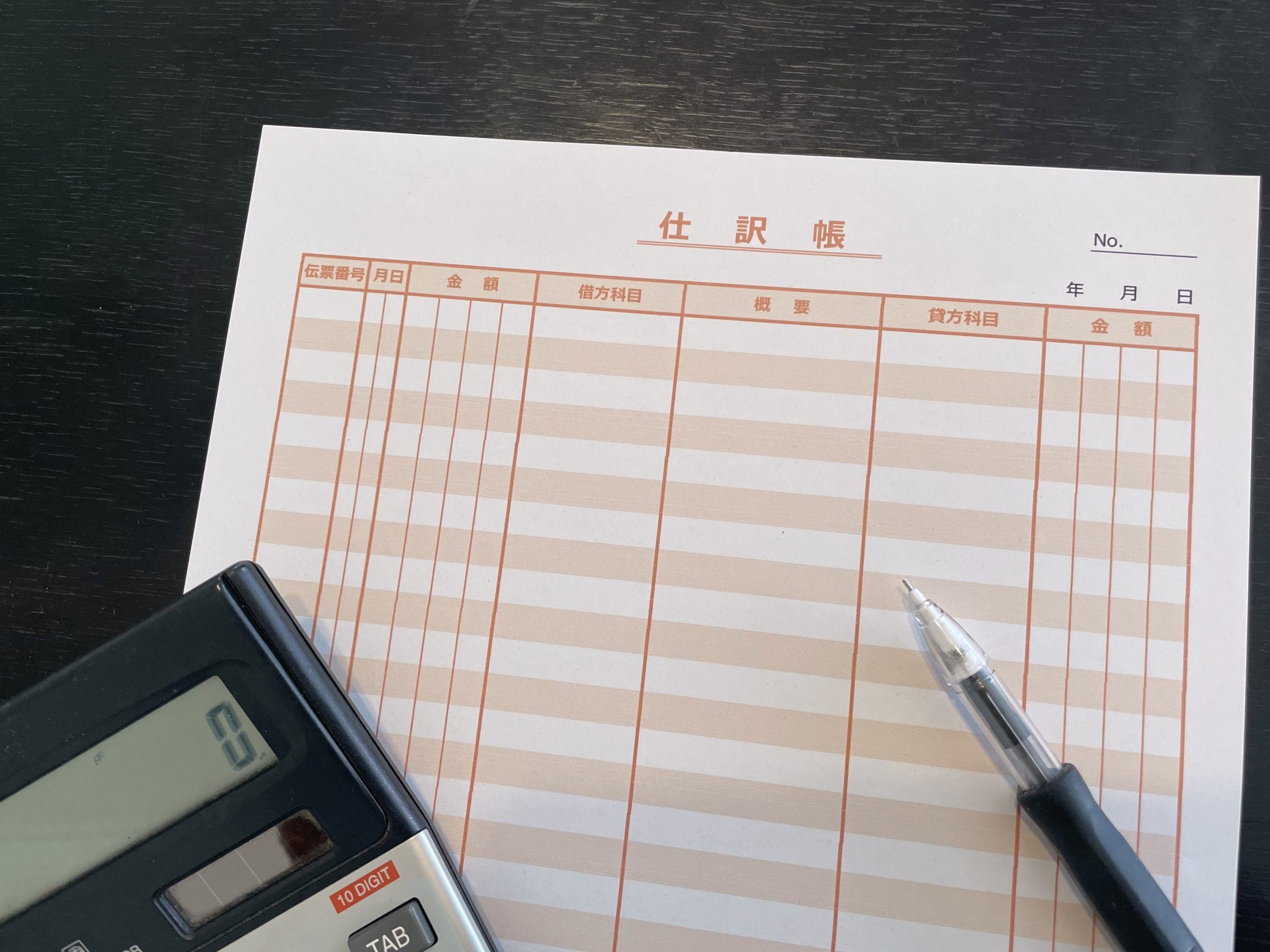 仕訳帳と電卓を使った経理業務のイメージ